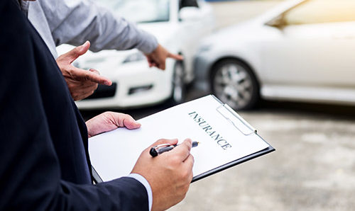 Insurance agent writing on clipboard while examining car after a car accident