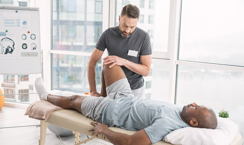 a person lying on a bed with his leg on the side getting a physical therapy treatment