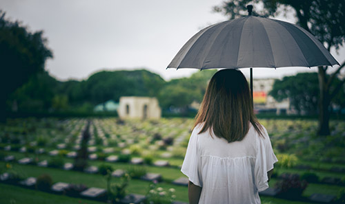 A woman holding an umbrella in a cemetery.