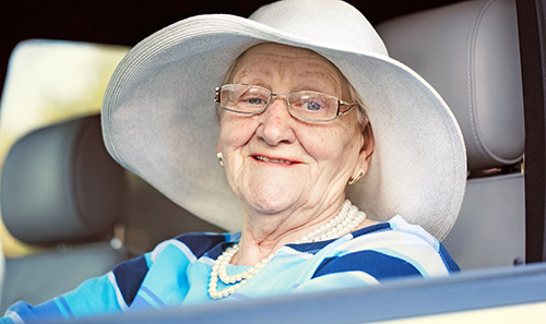 An elderly woman in a white hat is sitting in the driver's seat of a car.