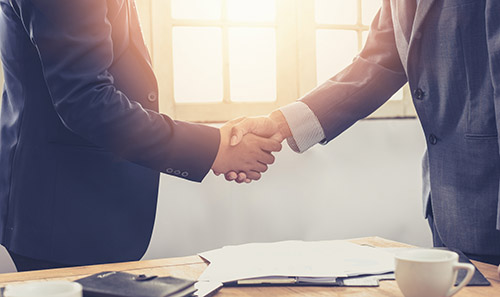 Two businessmen shaking hands at a desk during a settlement negotiation